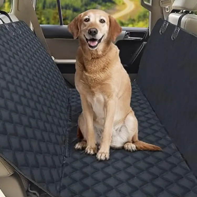 A happy dog relaxes on a Dog Seat Cover in the cars backseat. The black quilted cover extends over the seats and door sides, with greenery visible through the window.