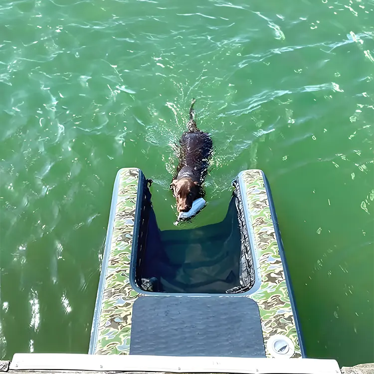 A brown dog swims through green water toward a camouflage-patterned Dog Water Ramp, carrying a toy.