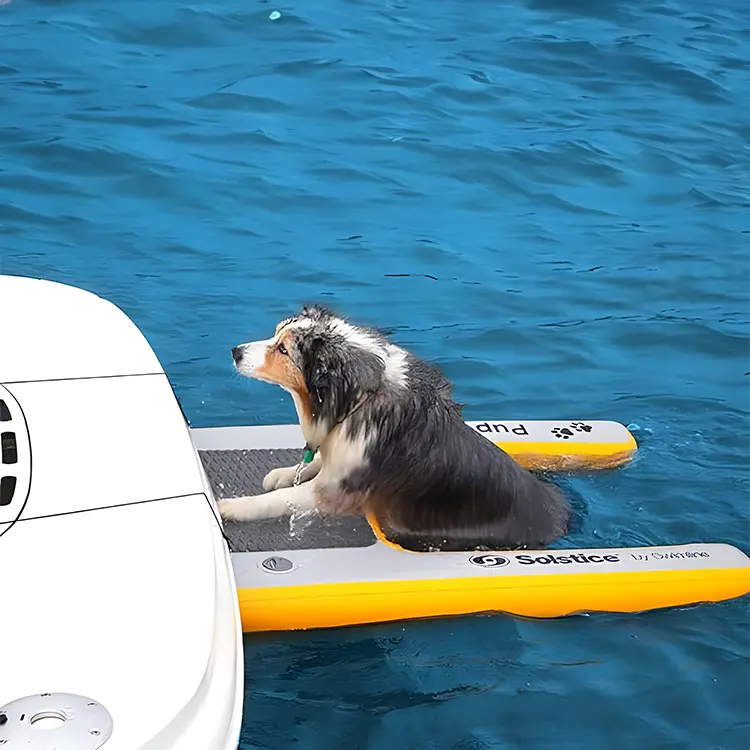 A wet dog lounges on a yellow and gray Dog Water Ramp in blue water, facing a white boat, appearing relaxed.